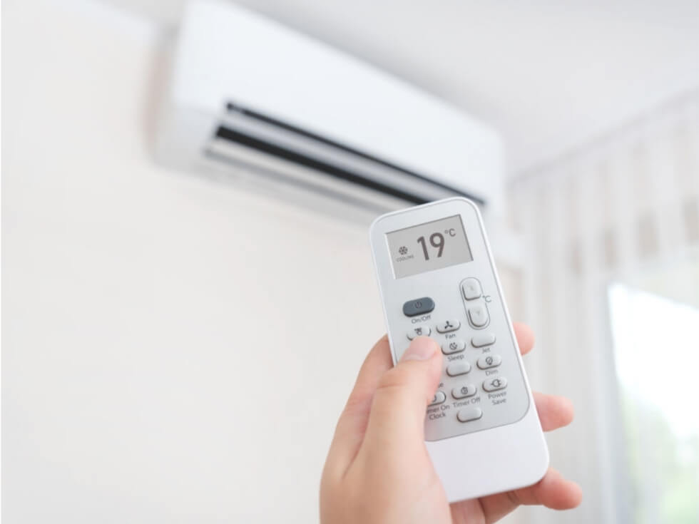 A person holding a remote control in front of an air conditioner.