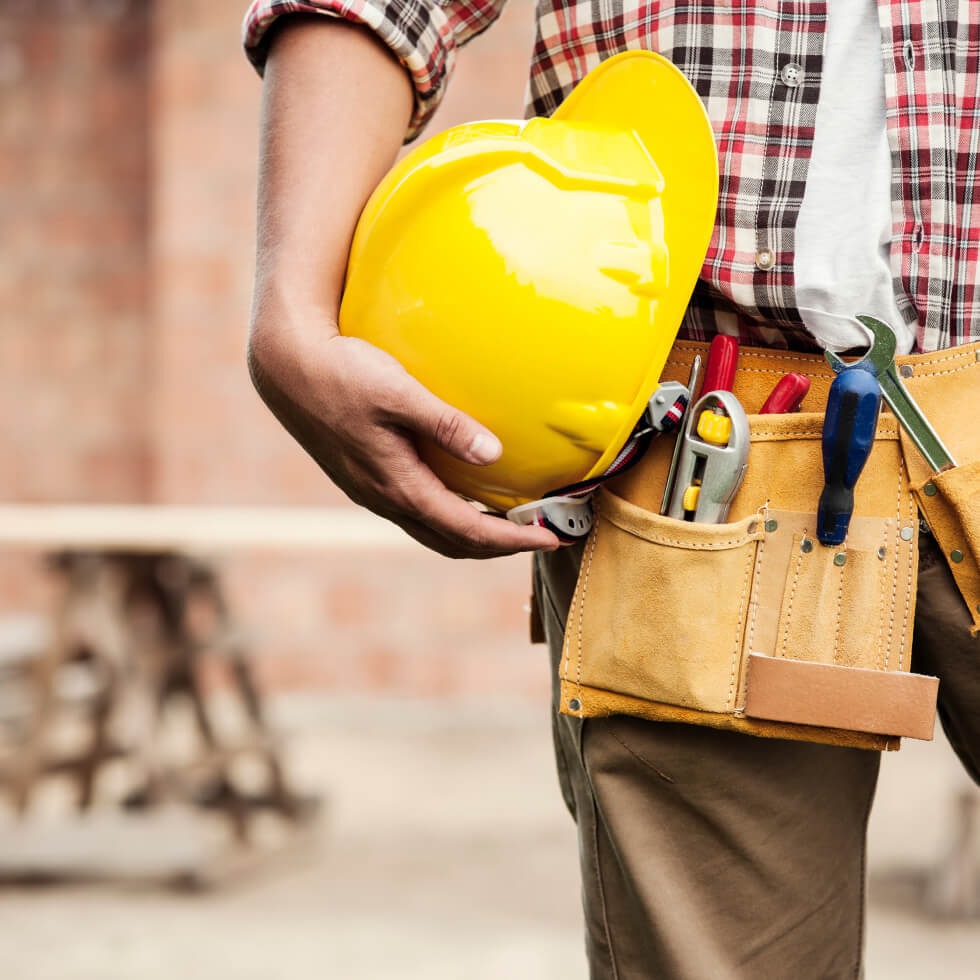 A builder holding a yellow hard hat and tools.