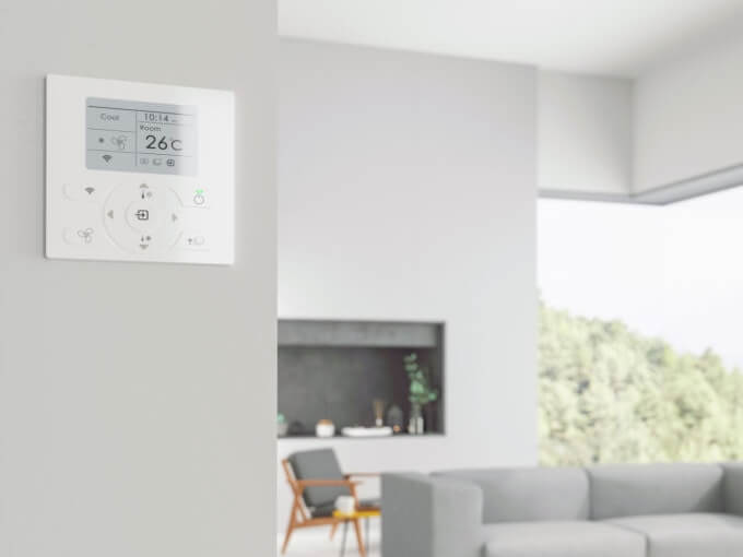 A white wall mounted thermostat in a living room equipped with air conditioning.