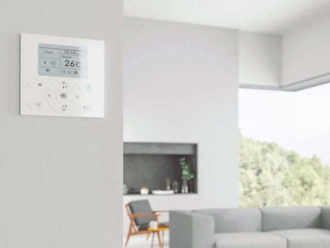 A white wall mounted thermostat in a living room equipped with air conditioning.