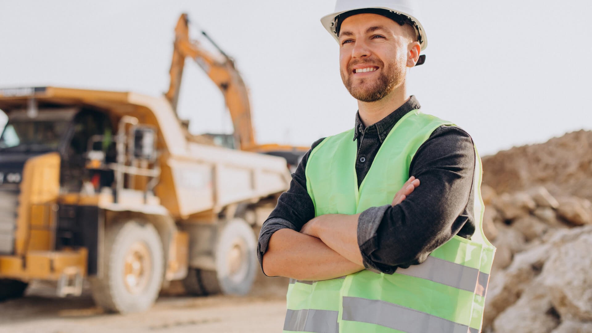 A builder with his arms crossed in front of a bulldozer.