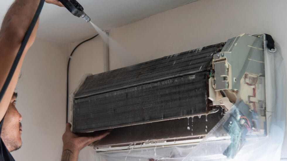 Technician cleaning an air conditioner unit.