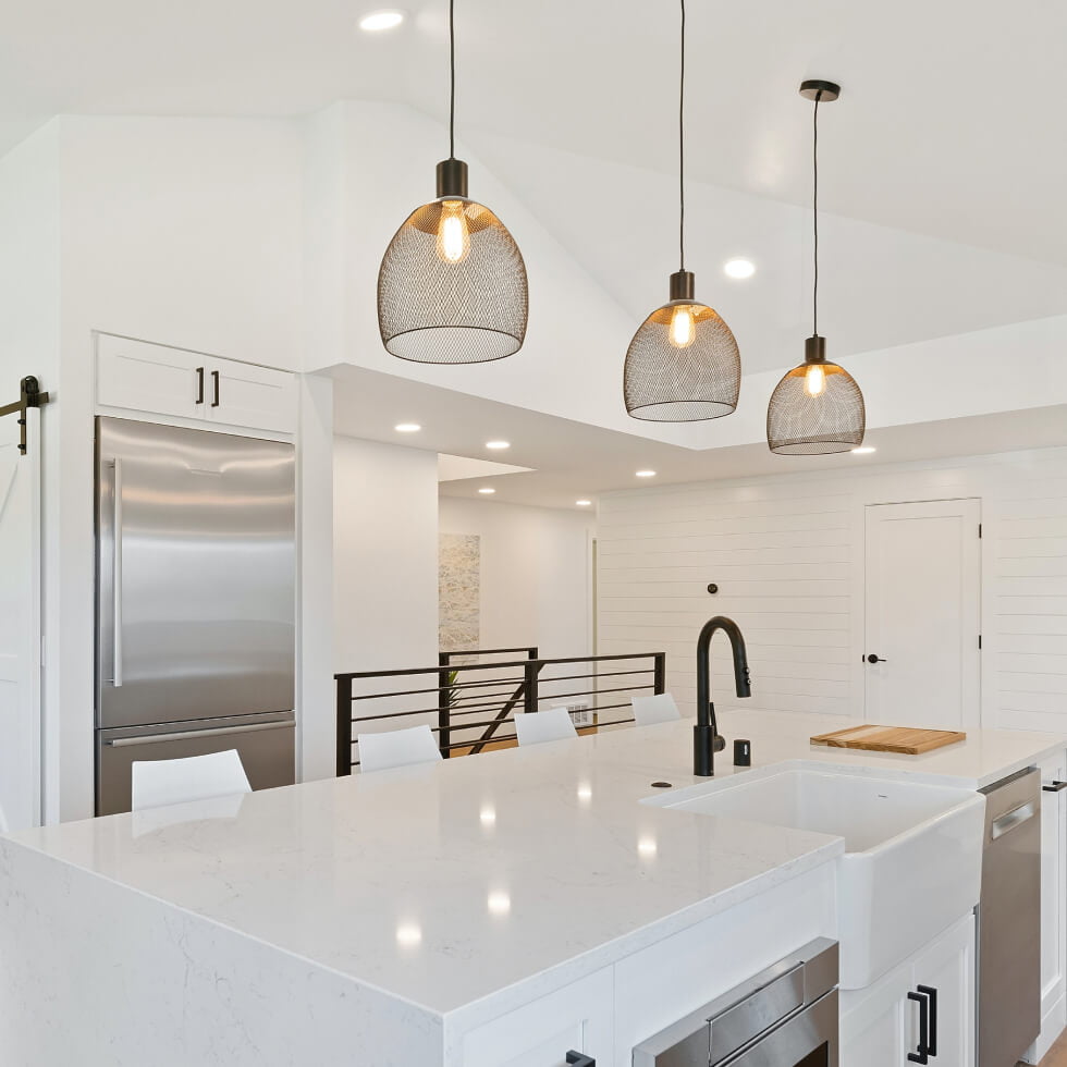 A white kitchen with stainless steel appliances and pendant lights, perfectly installed by expert electricians on the Sunshine Coast.