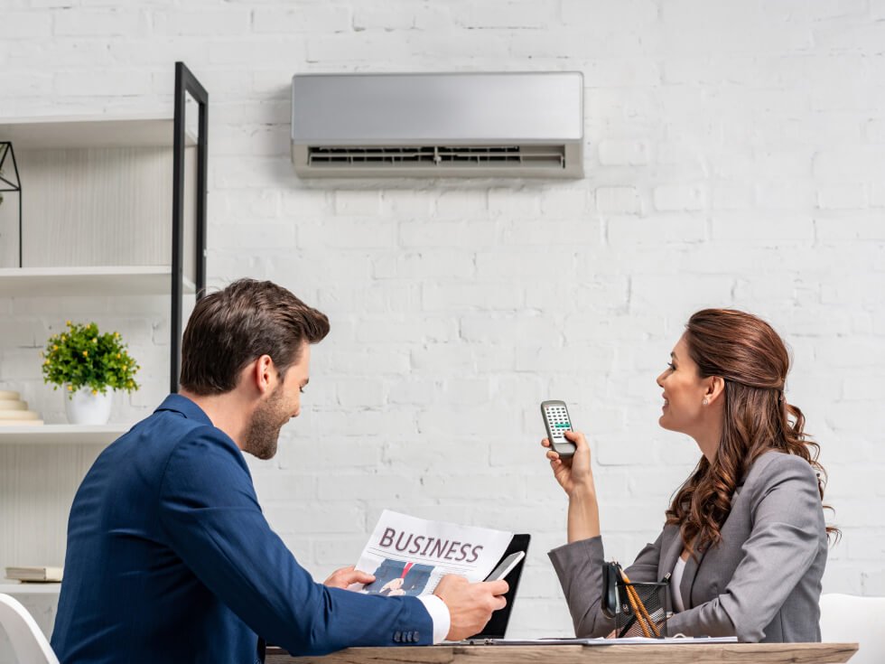 A man and woman are sitting at a table with an air conditioner.