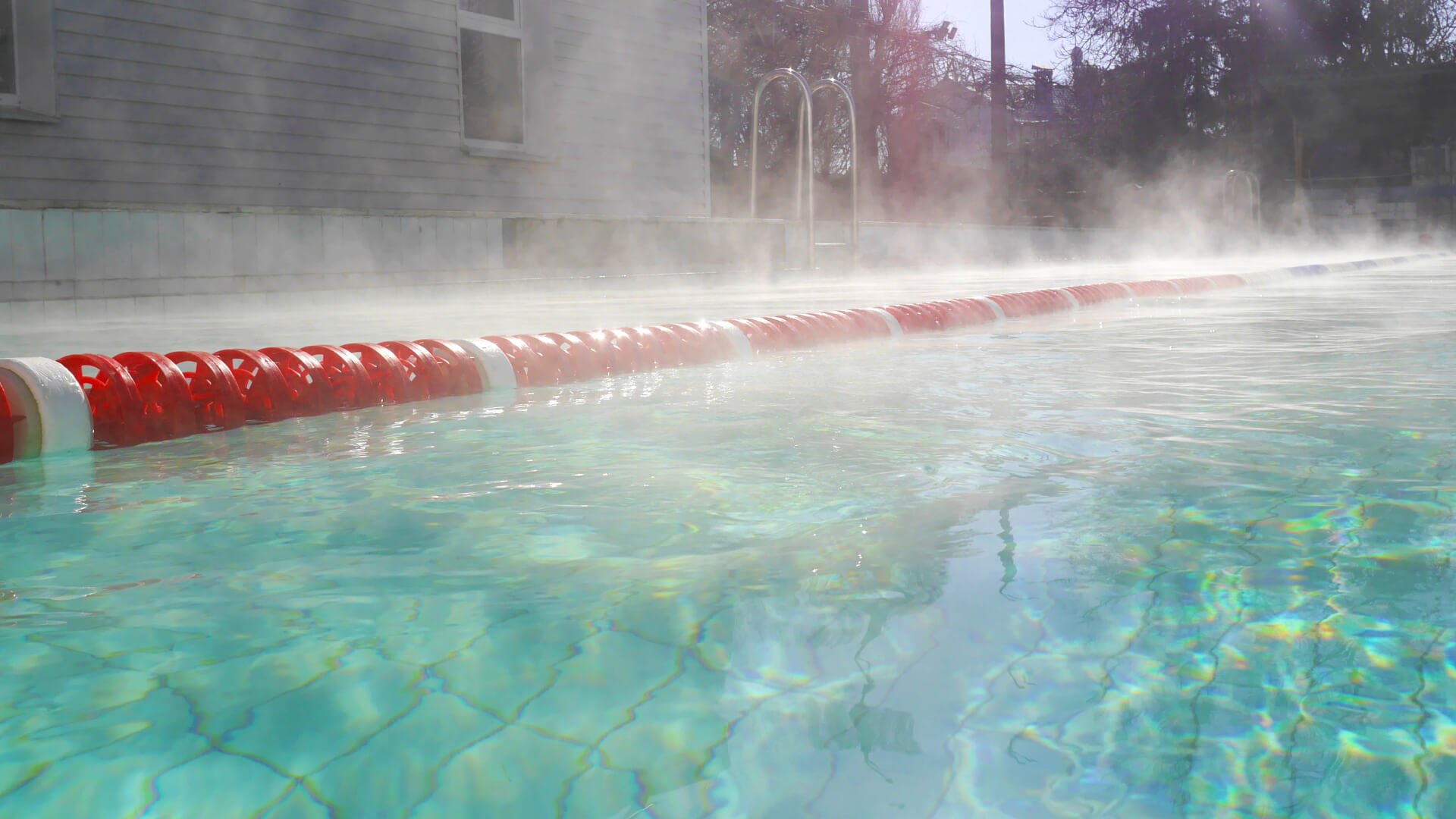 A swimming pool with visible billowing steam rising from the warm water and a red and white floating lane divider.