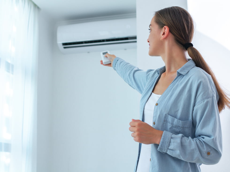 A woman is pointing at a Split System air conditioner with the remote control.