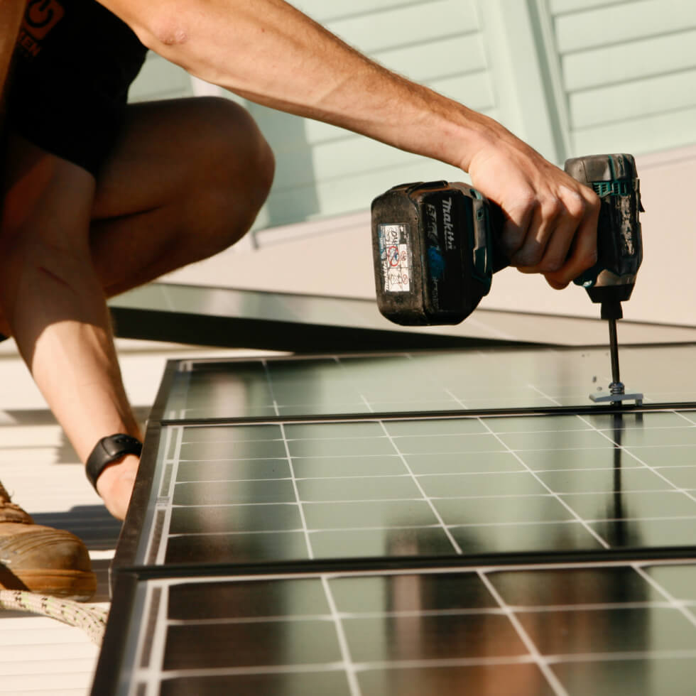 A man is using a drill on a solar panel on the Sunshine Coast.