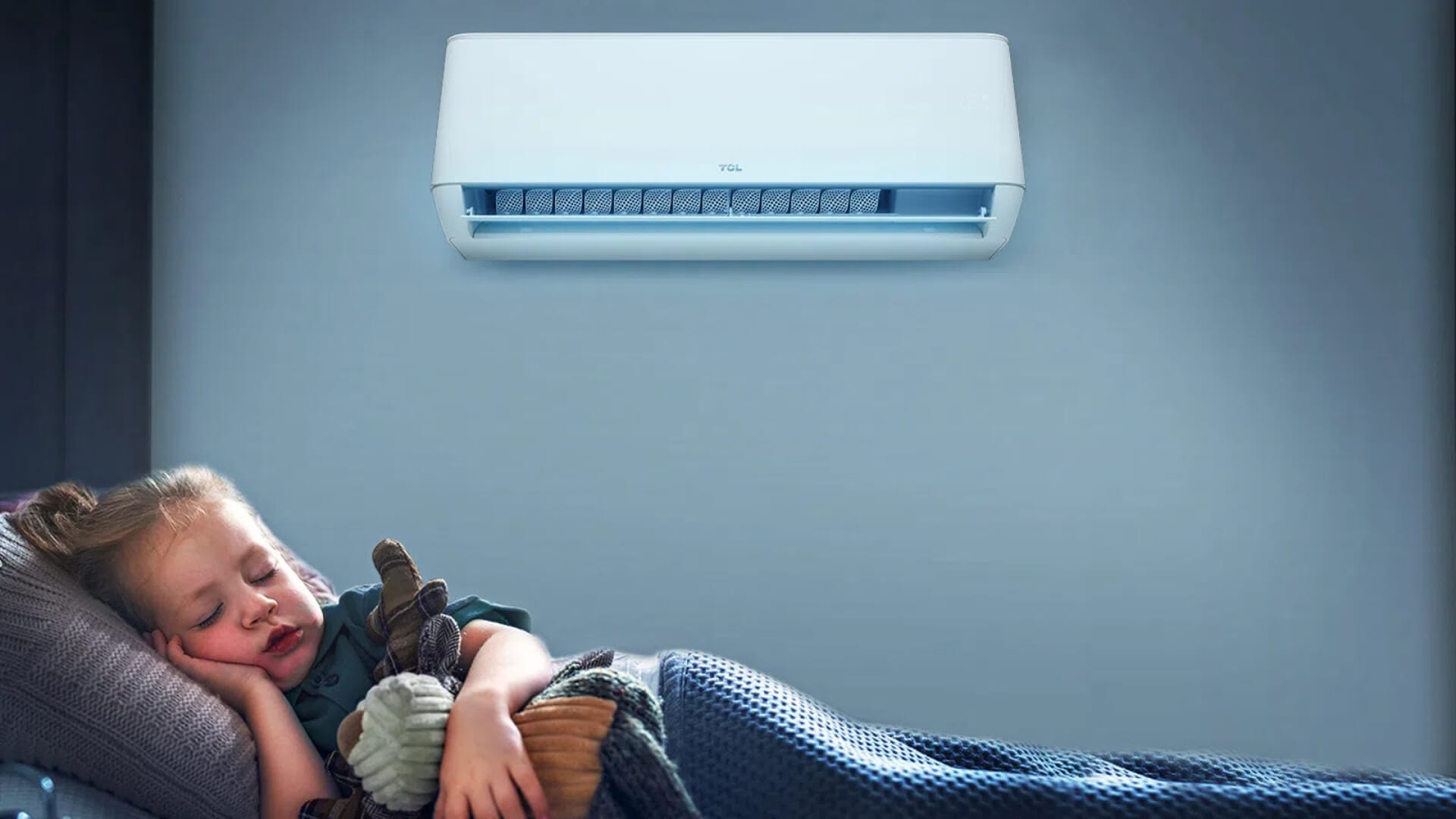 Child sleeping peacefully under a blanket in a room with a wall-mounted air conditioner above.