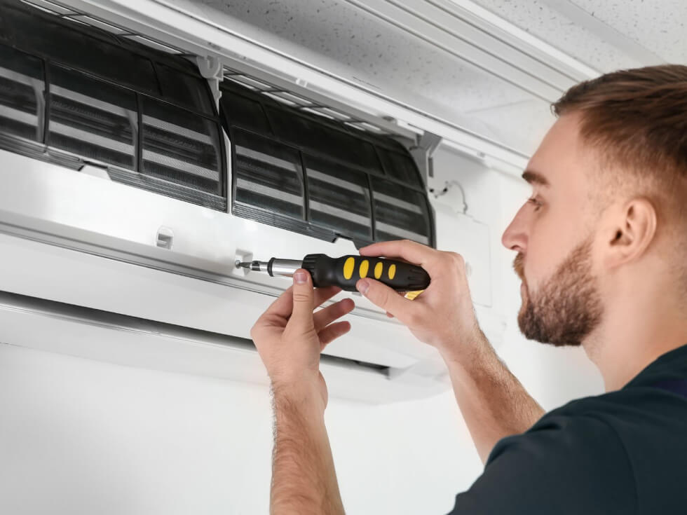 A man using a screwdriver to fix an air conditioner.