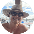 A woman wearing a hat and sunglasses at a dock.