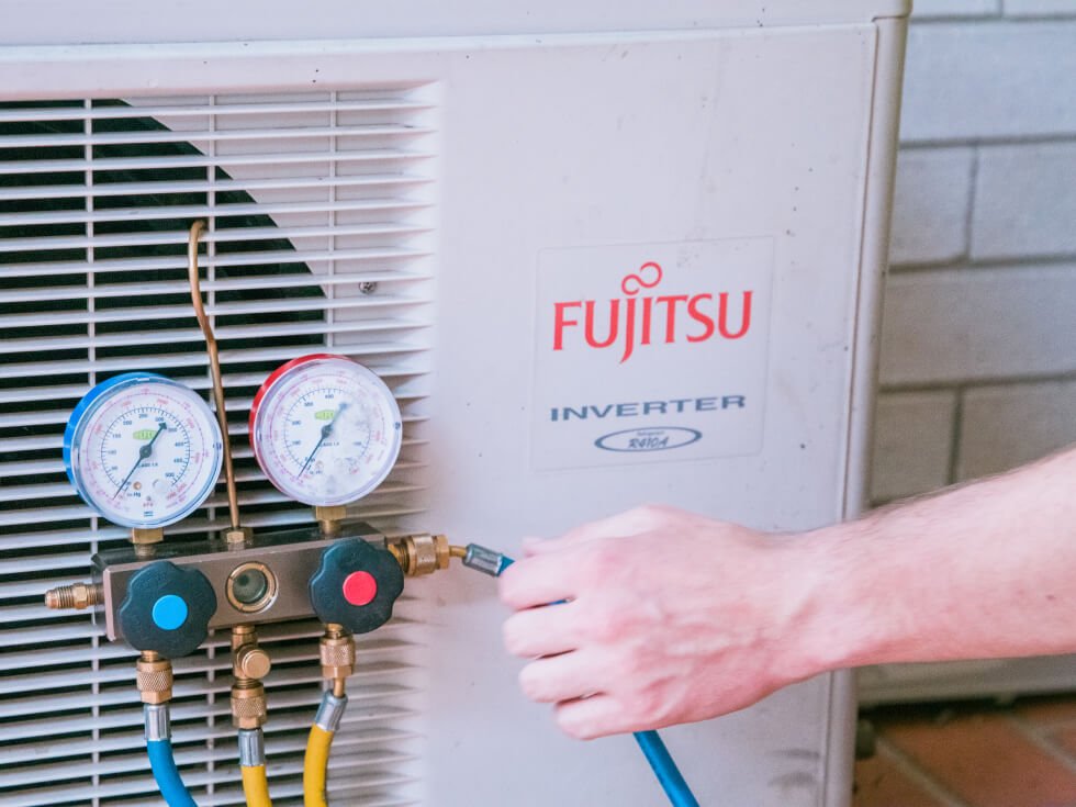 A man is working on a fujitsu air conditioner condenser.