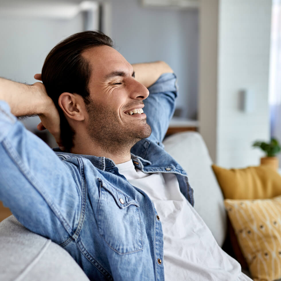 A man is relaxing on a couch at home, enjoying the comfort of air conditioning.