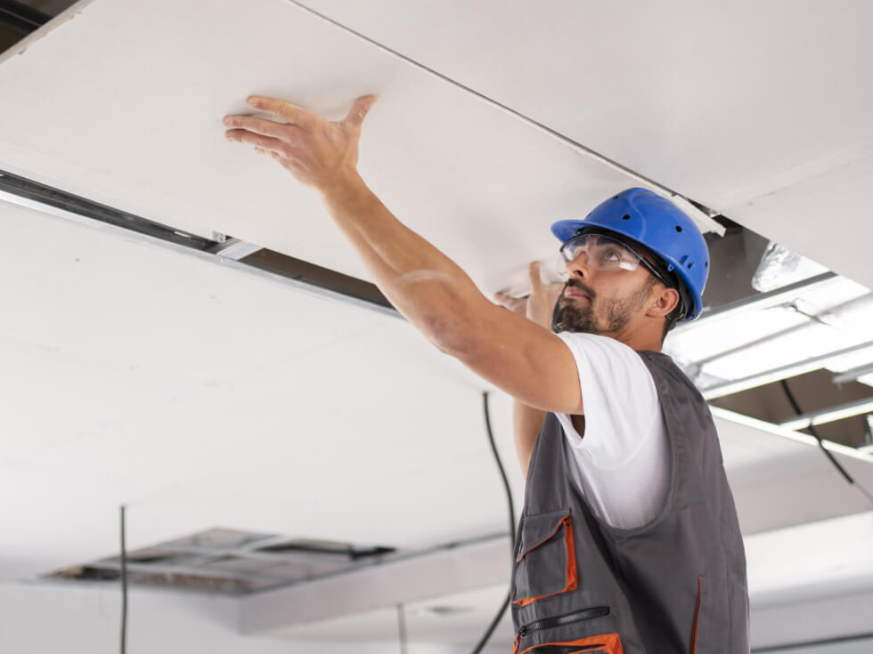 A construction worker is installing a ceiling in a building.