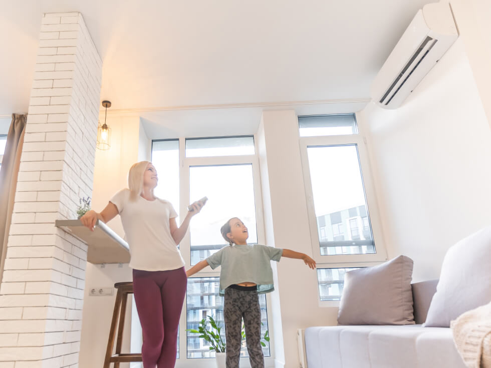 A woman and a child standing in a room with an air conditioner.