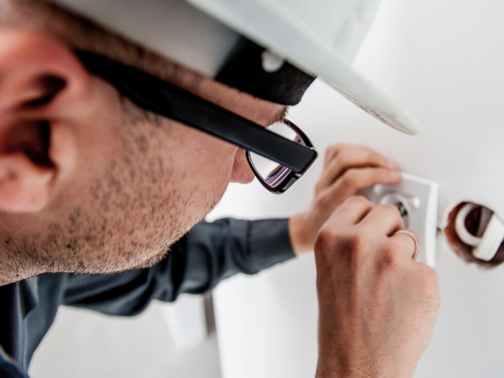 A man in a hard hat is fixing a light switch.
