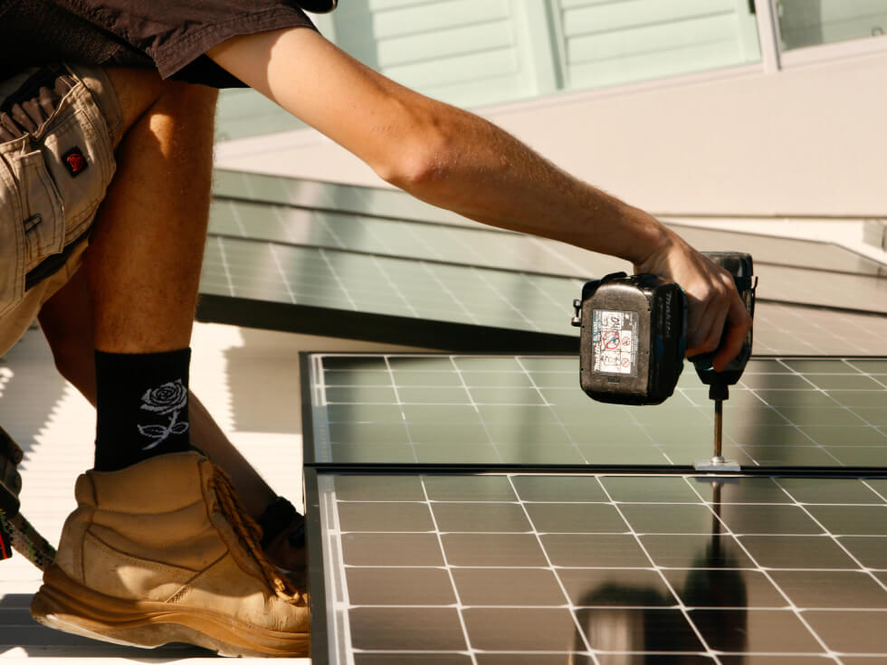 A man using a drill to fix a solar panel.