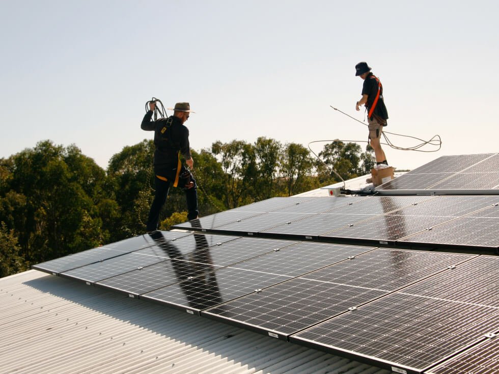 Two men working on solar panels on a roof.