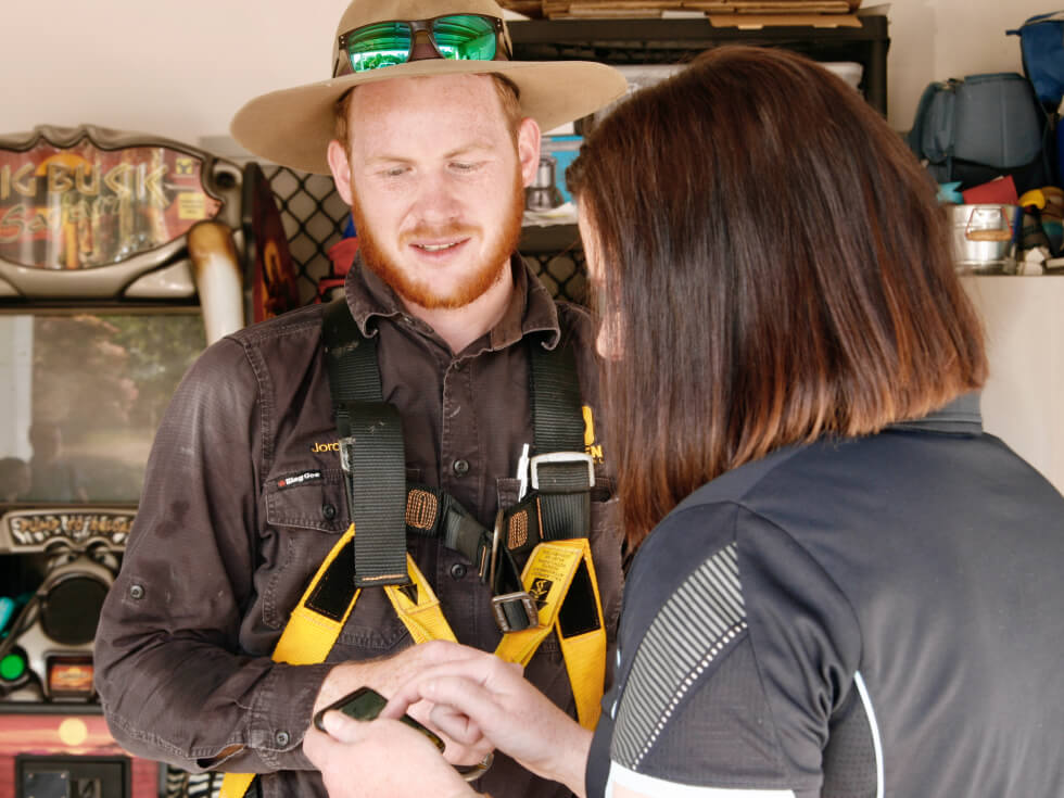 A solar technician man in a hat talking to a woman touching her phone.