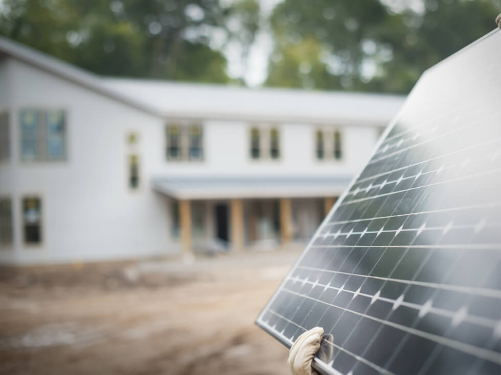 A man holding a solar panel in front of a house.