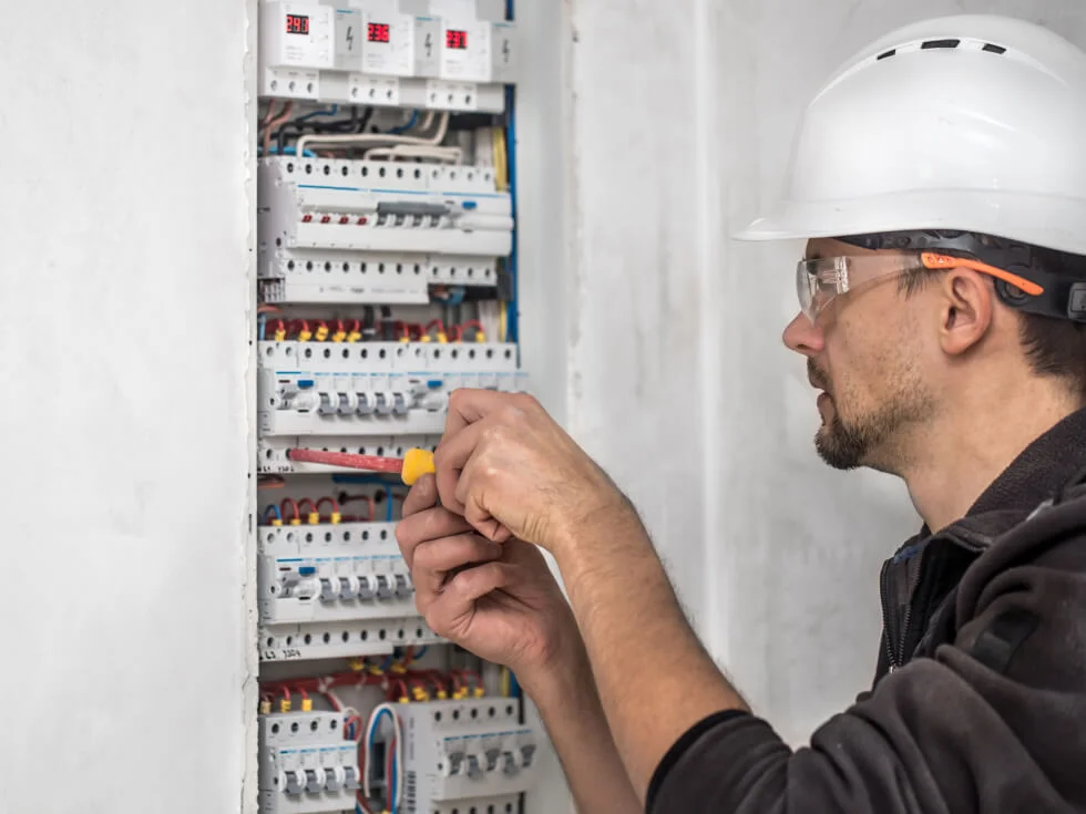 An electrician in a hard hat is working on an electrical panel.
