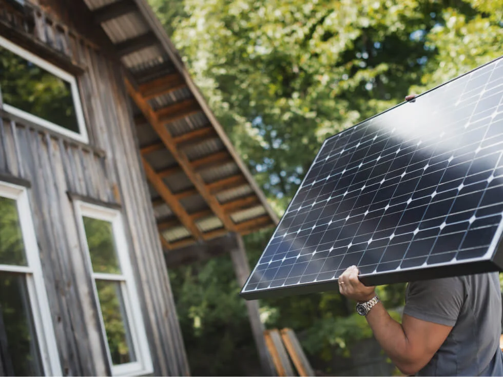 A man holding a solar panel in front of a house.