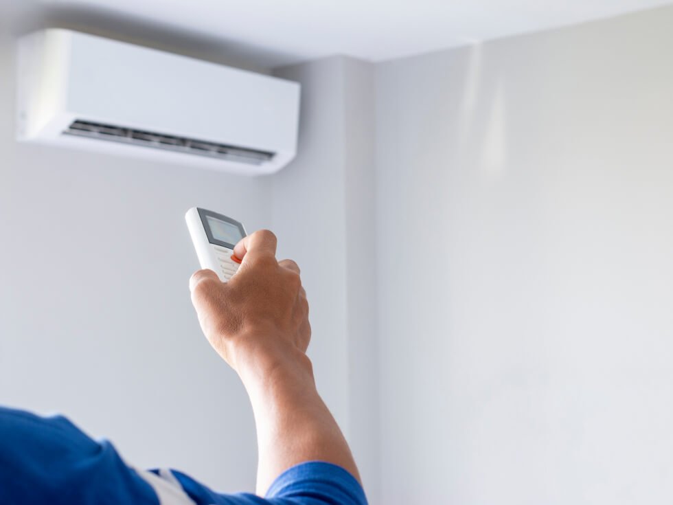 A man using a remote control to control an air conditioner.