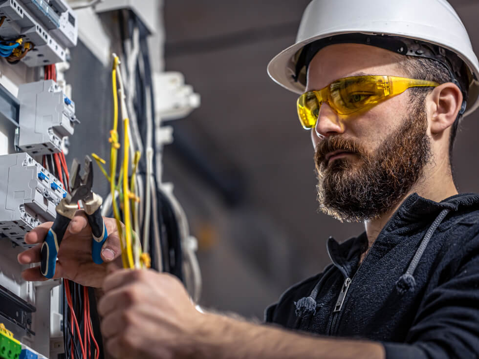 A man in a hard hat is working on electrical equipment.